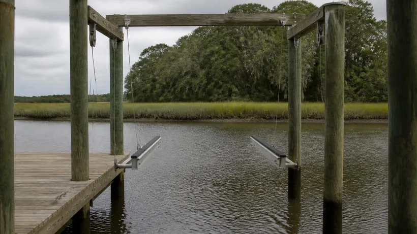 Empty boat lift cradle hanging on cables between dock pilings above a tidal creek