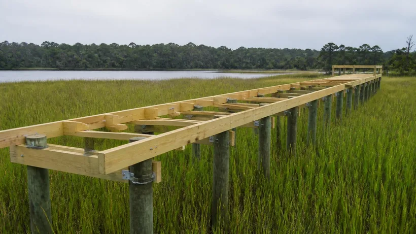 New dock framing on driven pilings over marsh grass, open joist bays not yet decked