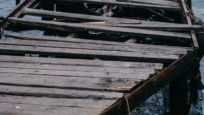 Failed timber dock decking with split and missing boards leaving gaps through to the water below