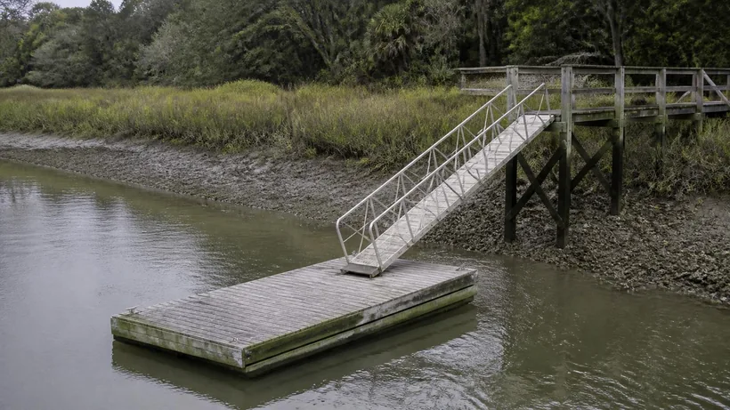 Aluminium gangway sloping steeply down to a timber float at low tide with pluff mud exposed along the bank